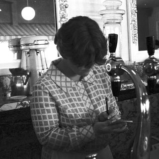Barista pouring coffee behind vintage counter.