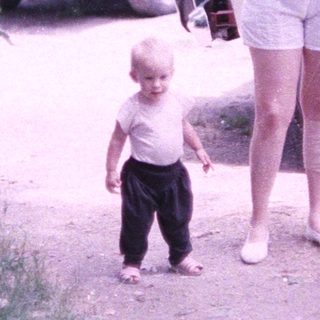 A woman and young child walking outdoors near parked vehicles.