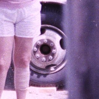 A woman and young child walking outdoors near parked vehicles.