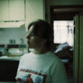 Blurred indoor kitchen scene with person wearing white shirt.