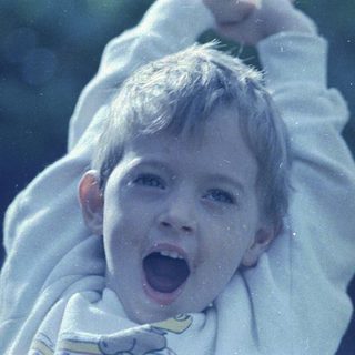 Child joyfully screaming outdoors, arms lifted.