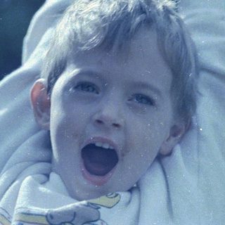 Child joyfully screaming outdoors, arms lifted.