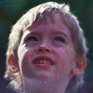 Child smiling upward, rain droplets in sunlight.
