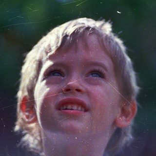 Child smiling upward, rain droplets in sunlight.