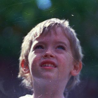 Child smiling upward, rain droplets in sunlight.