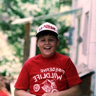 Boy smiling in rain wearing red shirt and cap.