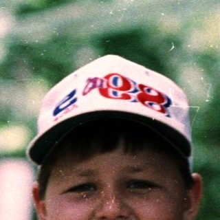 Boy smiling in rain wearing red shirt and cap.