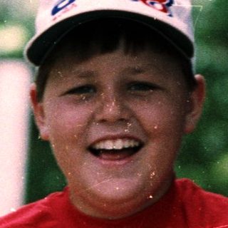 Boy smiling in rain wearing red shirt and cap.