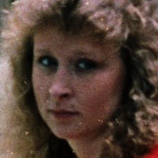 Woman in red shirt leaning on balcony railing.