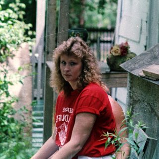 Woman in red shirt leaning on balcony railing.