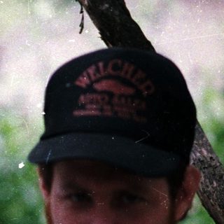 Two men in baseball caps posing outdoors during rain.