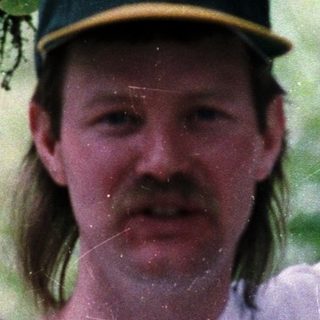 Two men in baseball caps posing outdoors during rain.