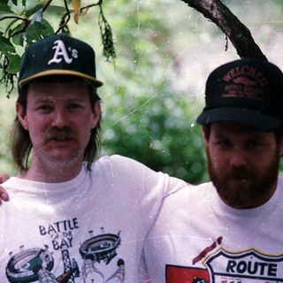 Two men in baseball caps posing outdoors during rain.