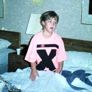Child in pink shirt with X on bed.
