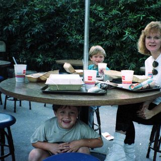 Family enjoying fast food outdoors at picnic tables.
