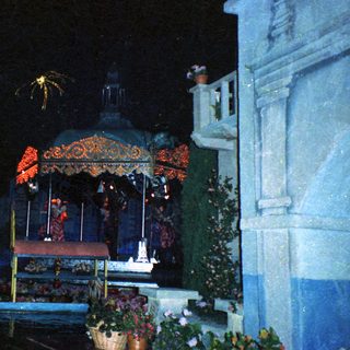 Nighttime religious procession with illuminated statue and fireworks.