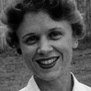 Woman smiling outdoors in 1960s-style blouse.