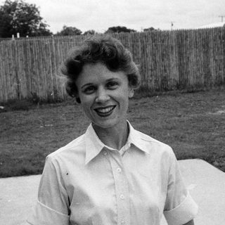 Woman smiling outdoors in 1960s-style blouse.