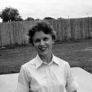 Woman smiling outdoors in 1960s-style blouse.
