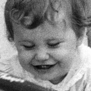 Baby smiling inside gated crib with stuffed toys.