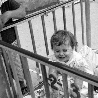 Baby smiling inside gated crib with stuffed toys.