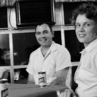 Two people smiling indoors, holding drinks.