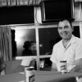 Two people smiling indoors, holding drinks.