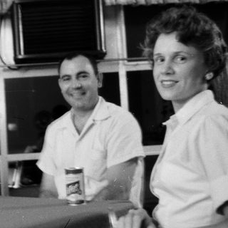 Two people smiling indoors, holding drinks.