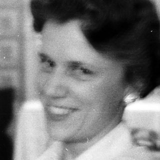 Black-and-white photo of smiling woman in kitchen.