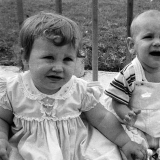 Two young children sitting, one crying, outdoors.