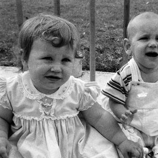 Two young children sitting, one crying, outdoors.