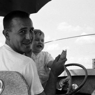 Family in vintage car, man holding baby, smiling.
