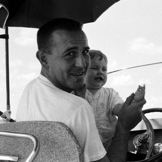 Family in vintage car, man holding baby, smiling.
