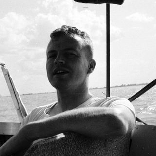 Man in naval uniform steering boat at sea.