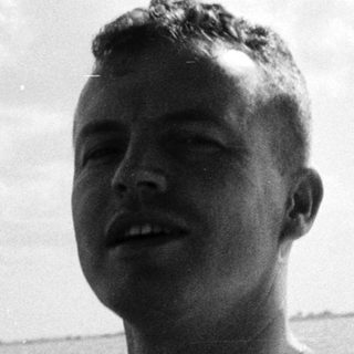 Man in naval uniform steering boat at sea.