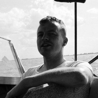 Man in naval uniform steering boat at sea.