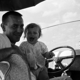 A man and young child laughing in vintage car.