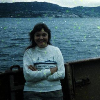 Person smiling on boat near coastal mountains.