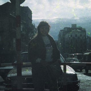 Urban scene with lone figure standing on bridge. Rainy cityscape.