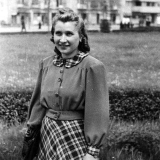 Young woman smiling outdoors in 1940s-style clothing.