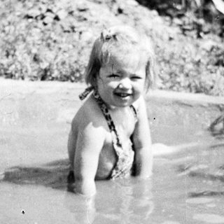 Young child smiling while playing in shallow water outdoors.