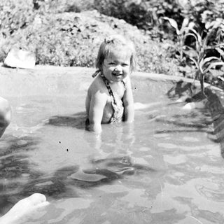 Young child smiling while playing in shallow water outdoors.