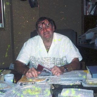 Man sitting at cluttered desk with papers.