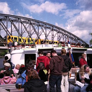 People boarding ferry under large bridge.