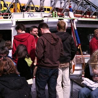 People boarding ferry under large bridge.