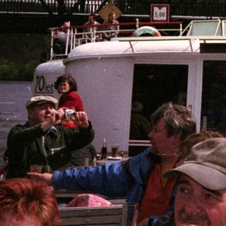 Boat tour with passengers under metal bridge.