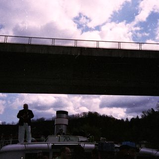 Person conducting boat under elevated bridge.