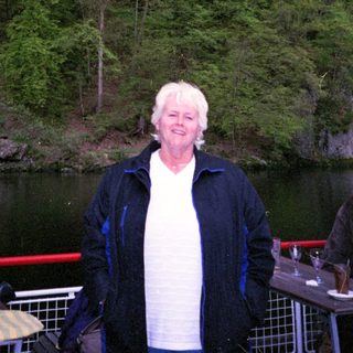 Woman standing by lake near forested hillside.