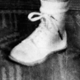 Young child holding umbrella indoors, dressed in diaper and overalls.