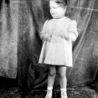 Young child in vintage dress standing indoors.